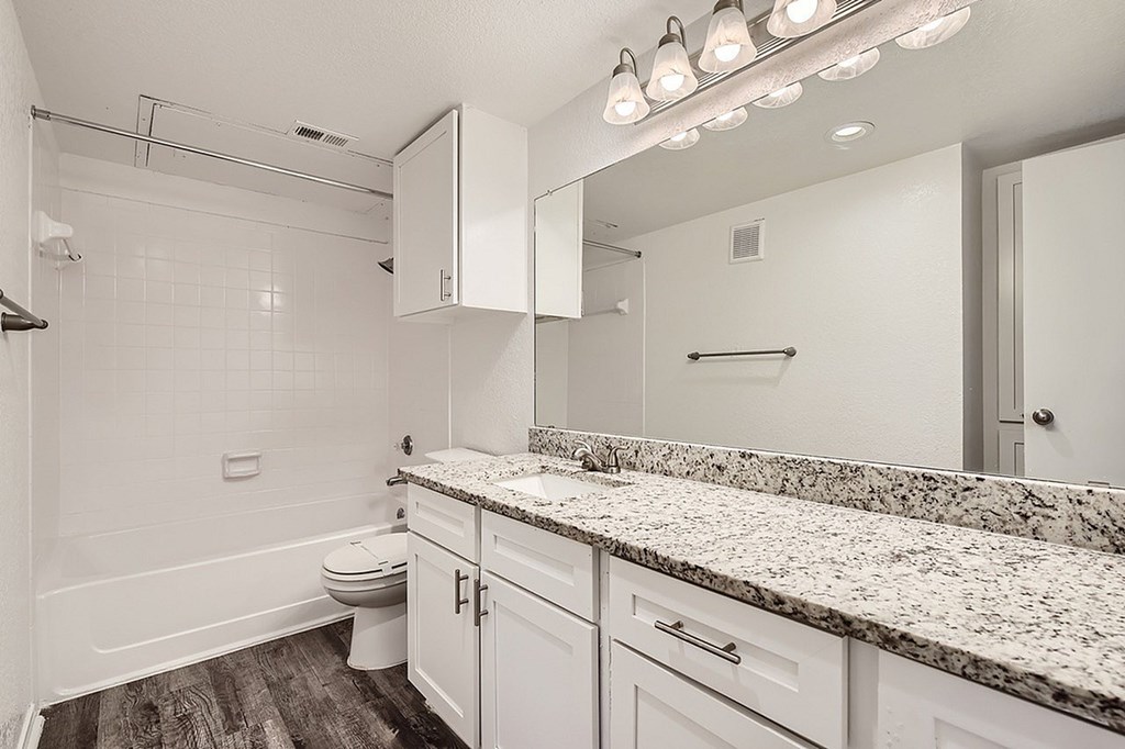 A white bathroom with a marble counter top and a walk in shower.