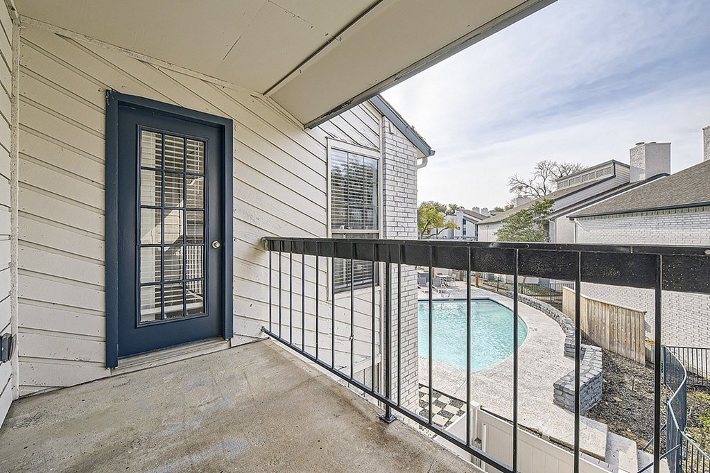 A balcony with a black railing and a blue door overlooks a pool.