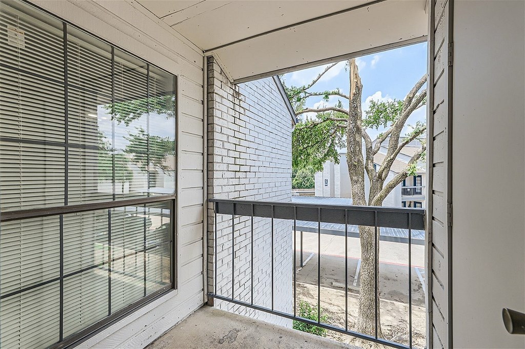 A balcony with a black railing and a view of a tree and a building.