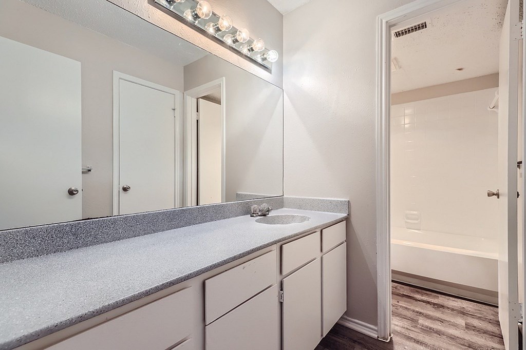 A bathroom with a vanity and a mirror with lights above it.