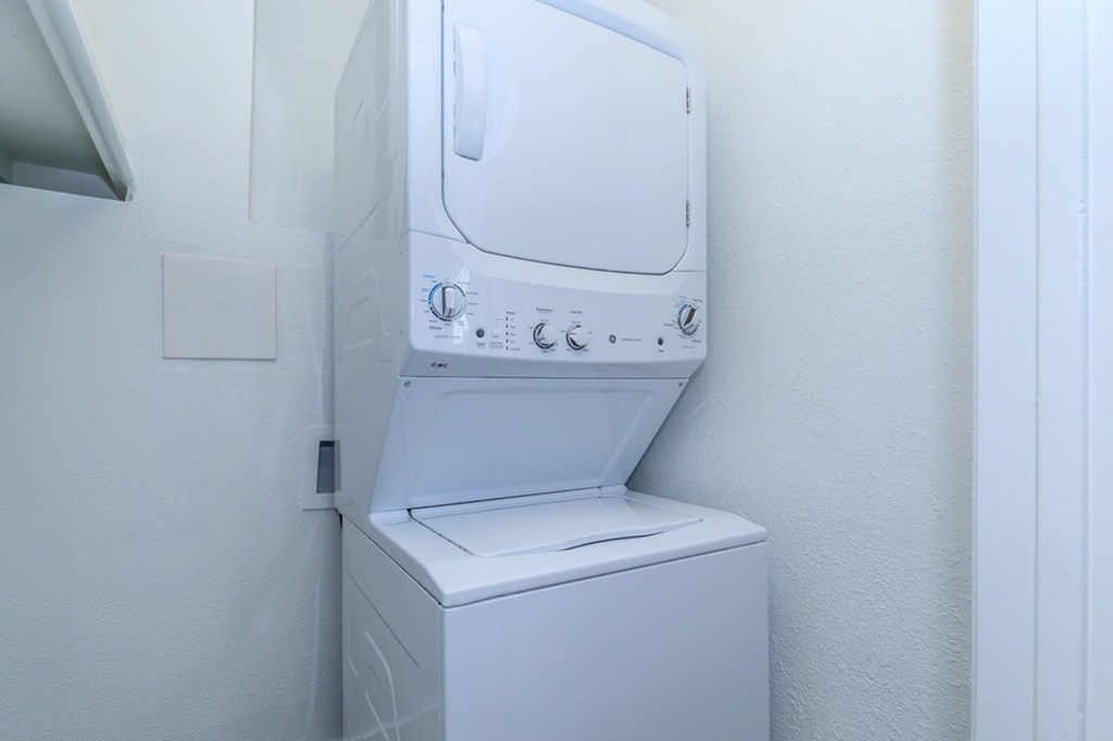A white dryer is sitting in a small, white-walled laundry room.