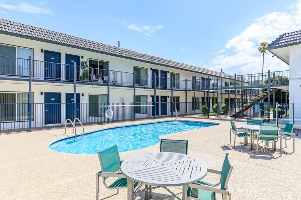A pool area with a table and chairs in front of a building.