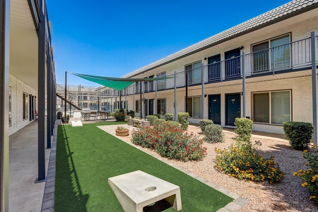 A sunny day at a modern apartment complex with a green lawn and a white bench.