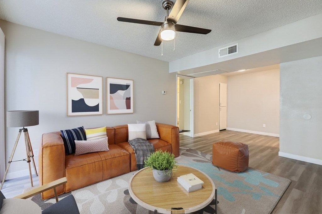 A living room with a brown leather couch, a wooden coffee table, and a ceiling fan.