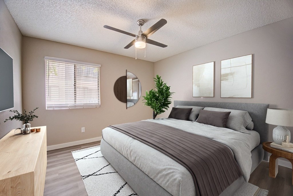 A bedroom with a large bed, a ceiling fan, and a potted plant.
