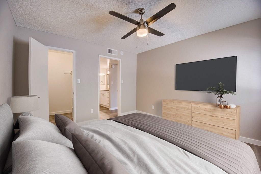 A bedroom with a bed, a ceiling fan, and a television mounted on the wall.