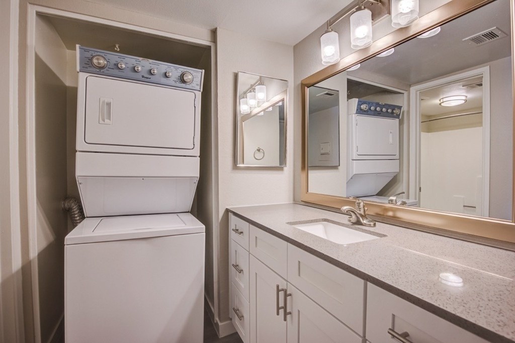 A white oven and dryer are in a small bathroom with a sink and mirror.