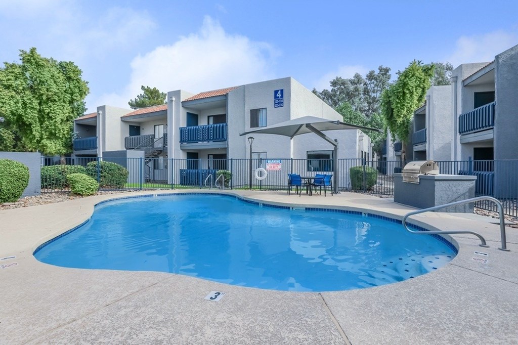 A swimming pool in front of a building with a blue sky and clouds in the background.