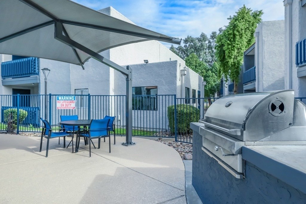 A BBQ grill is on a patio with a blue chair and table.