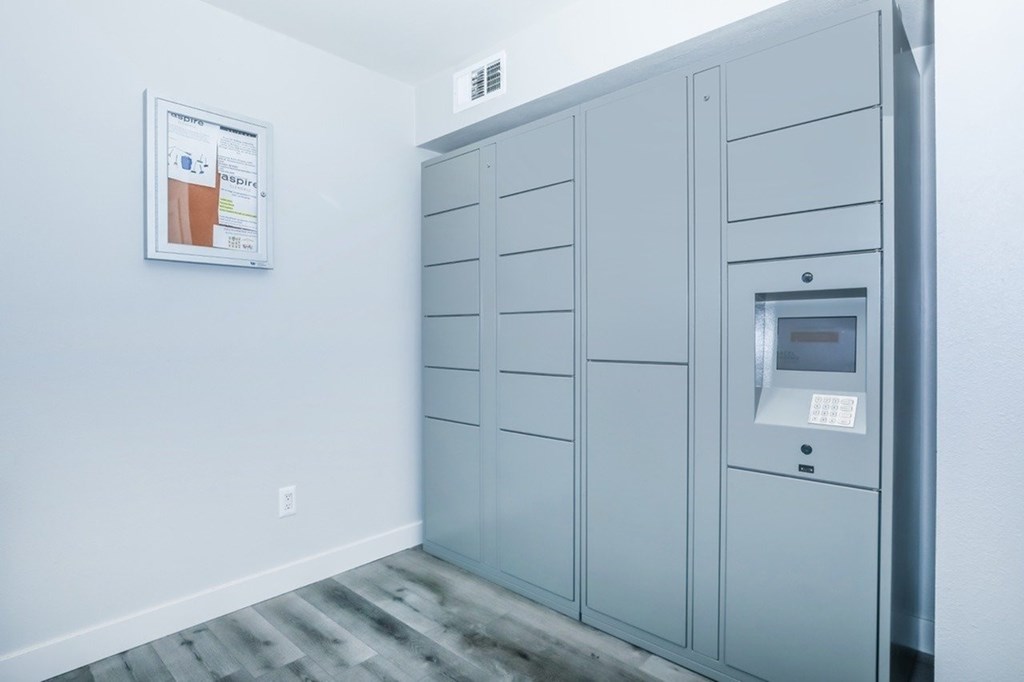 A wall-mounted locker with a door and a keypad is in a room with a poster on the wall.