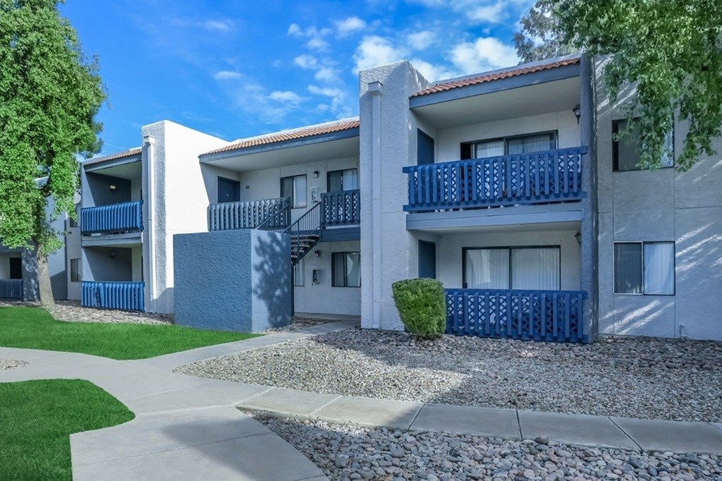 A white building with blue railings and a small bush in front.