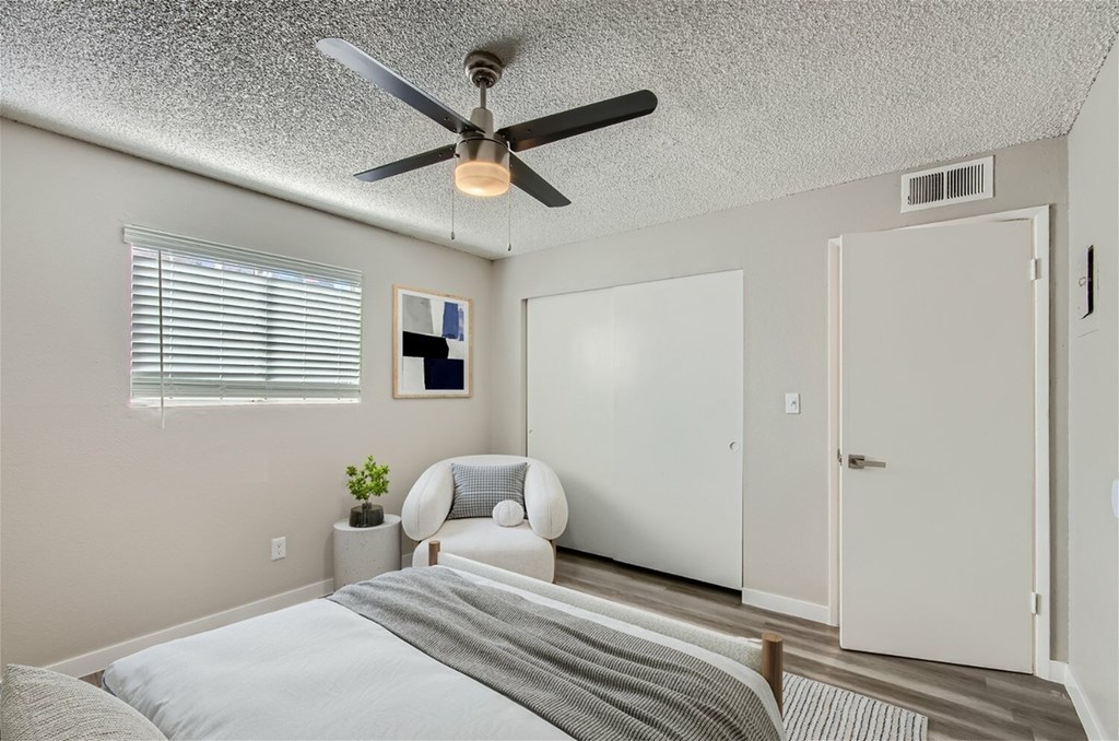 A bedroom with a bed, chair, and a ceiling fan.