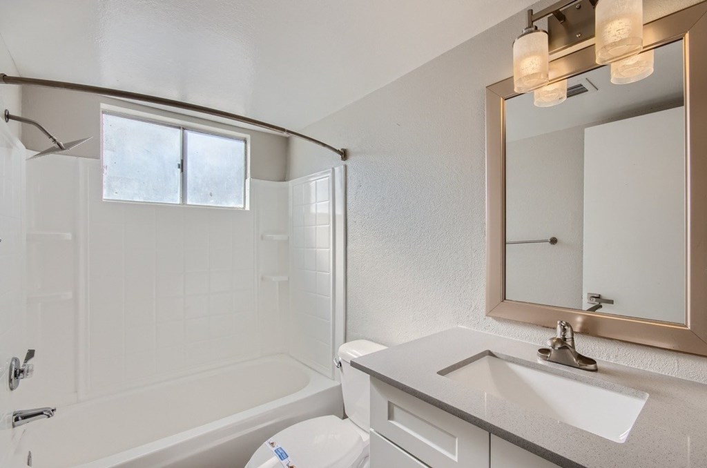 A white bathroom with a tub, sink, mirror, and light fixture.