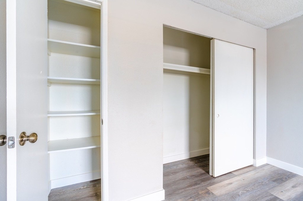 A white door with a gold handle is open to a room with a white wall and a white closet with shelves.