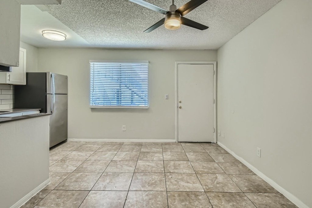 A kitchen with a refrigerator, a ceiling fan, and a door.