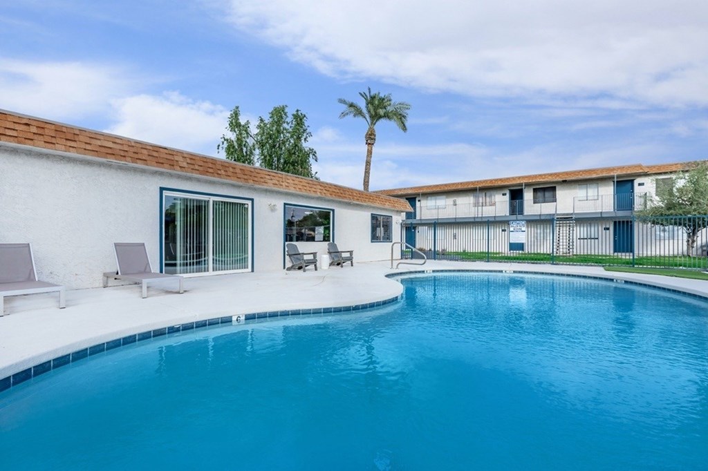 A swimming pool in a backyard with a white house and a palm tree.