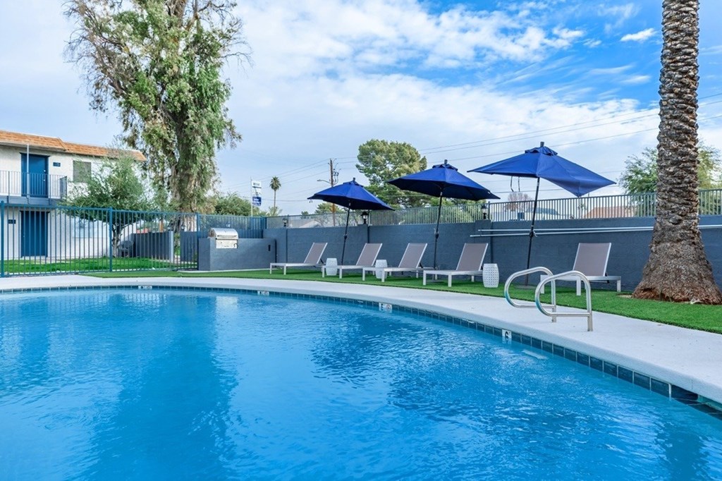 A pool with blue water and sun loungers under blue umbrellas.