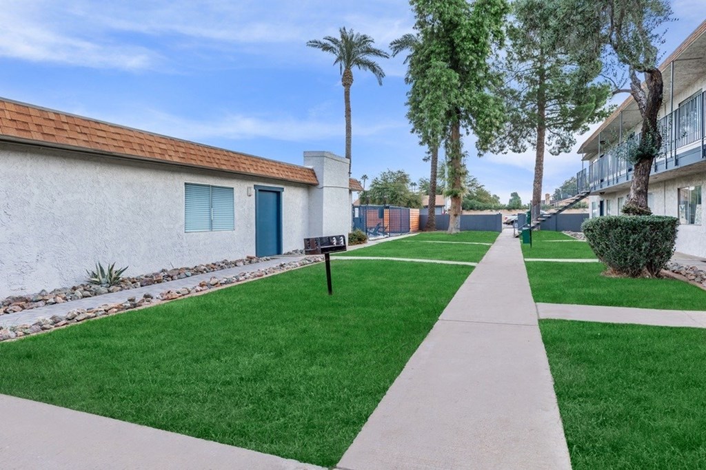 A white building with a blue door is on the left side of a walkway.