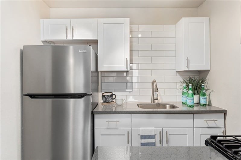 A modern kitchen with a stainless steel refrigerator and white cabinets.