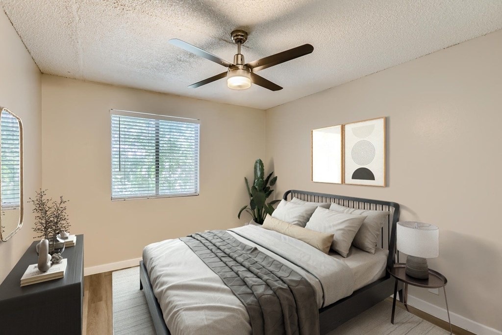 A bedroom with a bed, a ceiling fan, and a small table with a lamp.