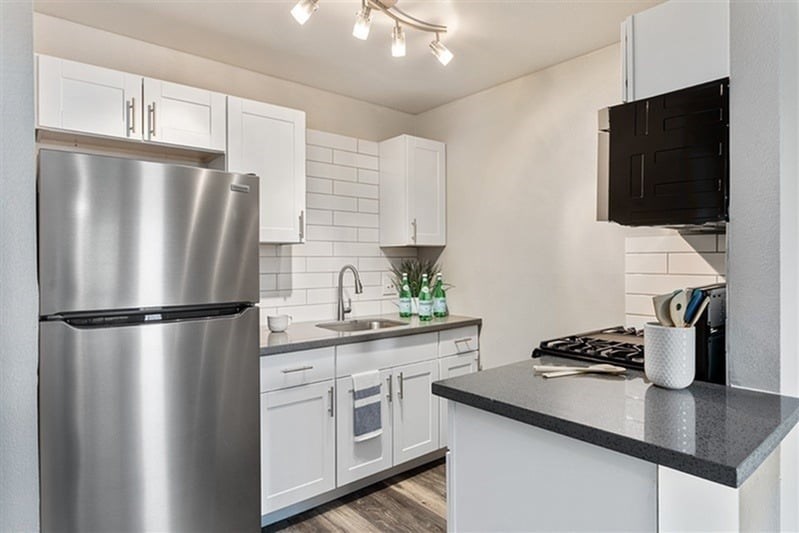 A modern kitchen with a stainless steel refrigerator and white cabinets.