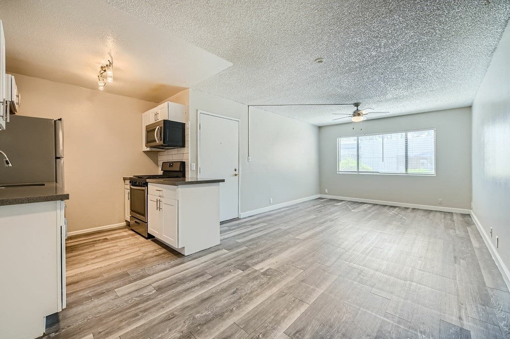 A sparsely furnished kitchen and living room with wood flooring.