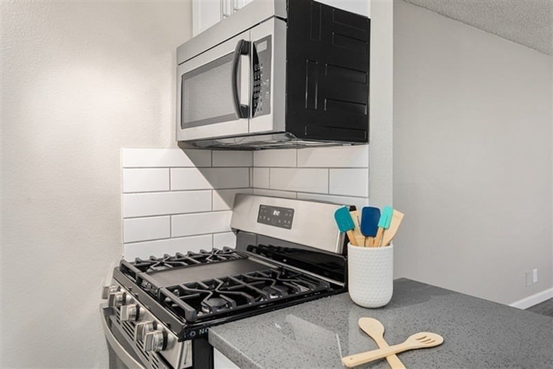 A modern kitchen with a black microwave above a stove and utensils in a cup.