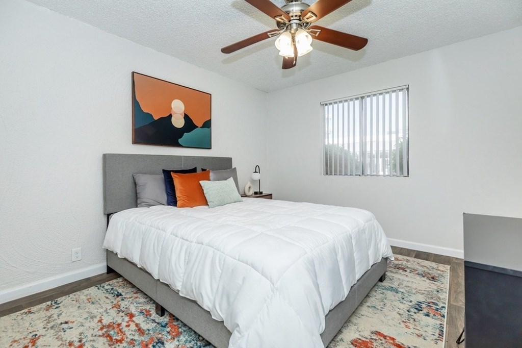 A bedroom with a bed, pillows, a ceiling fan, and a painting on the wall.