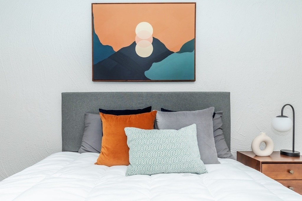 A bed with a grey headboard and a painting above it.