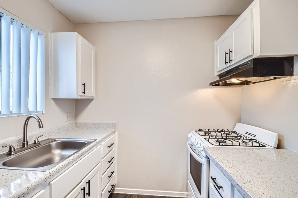 A kitchen with a stove, sink, and cabinets.