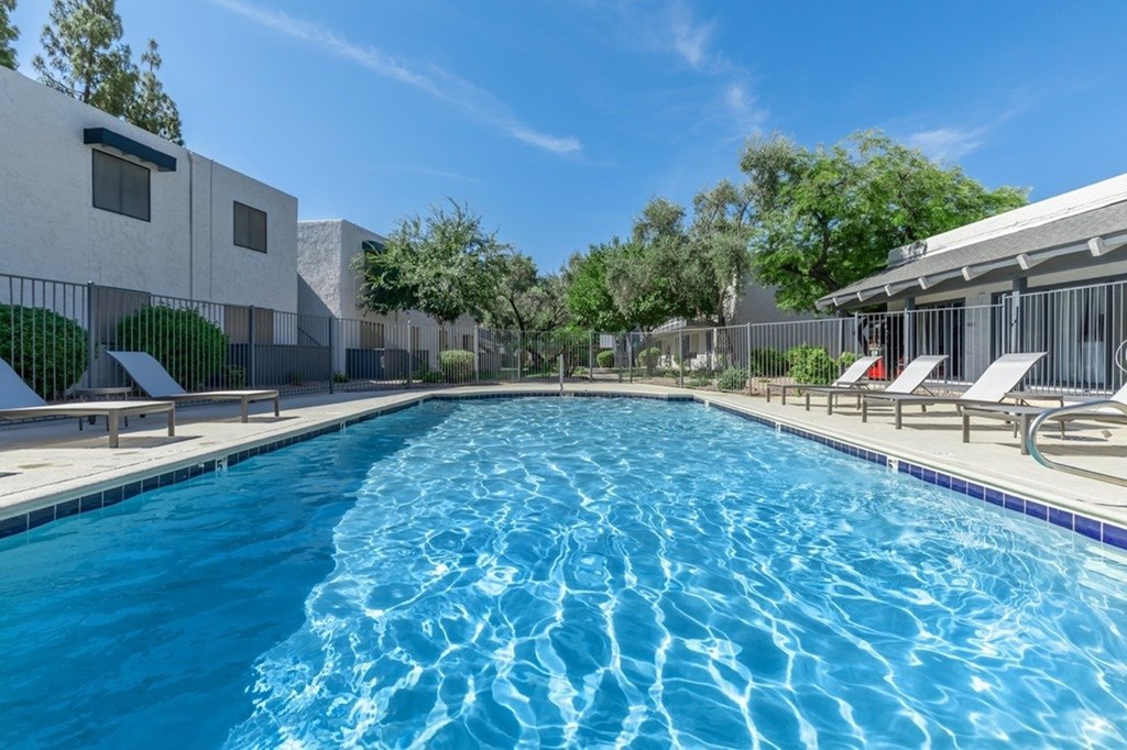 A swimming pool with a blue tiled edge and sun loungers on the side.