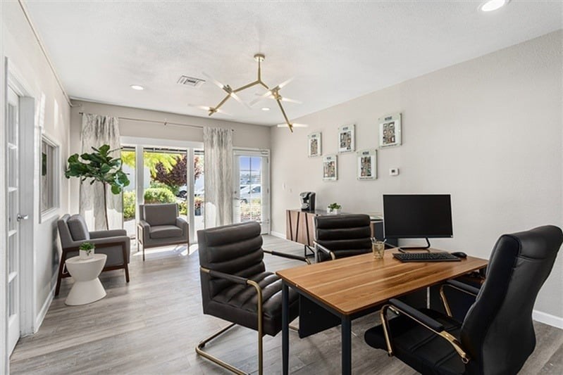 A modern home office with a wooden desk and black chairs.