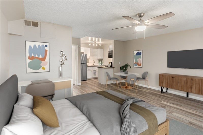 A modern bedroom with a large bed and a kitchen area in the background.