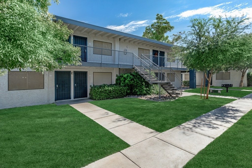 A sunny day at a residential complex with a building, green lawn, and a concrete pathway.