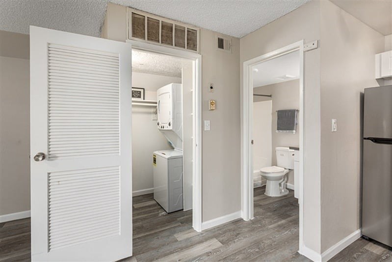 A white door is open to a bathroom with a toilet, sink, and a small refrigerator.