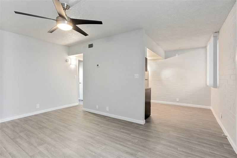 A room with a ceiling fan and light fixture, and a white wall with a doorway leading to another room.