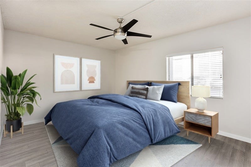 A bedroom with a bed, a ceiling fan, and a potted plant.