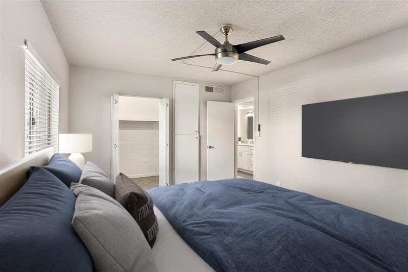 A bedroom with a bed, pillows, and a ceiling fan.
