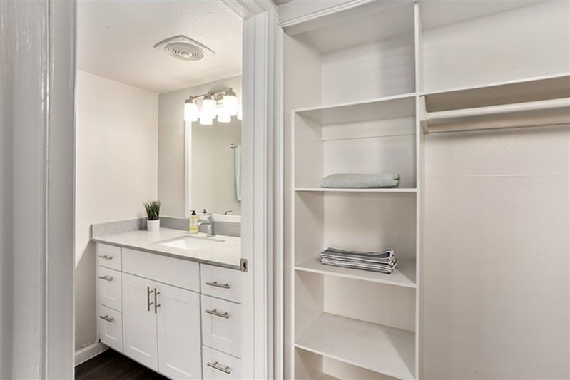 A white bathroom with a mirror, sink, and shelves.