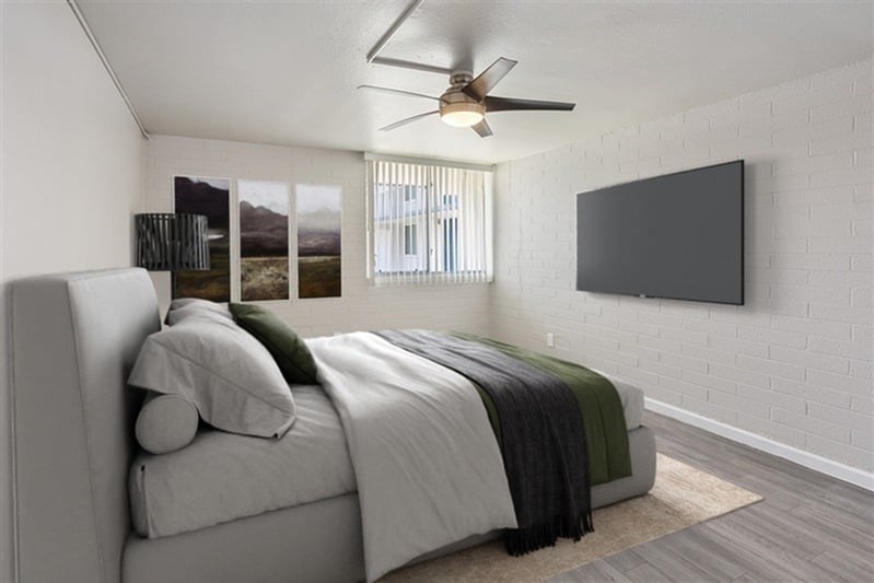 A bedroom with a bed, a ceiling fan, and a flat screen TV mounted on the wall.