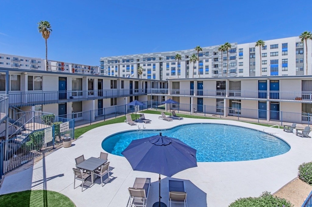 A pool area with a blue umbrella and chairs.
