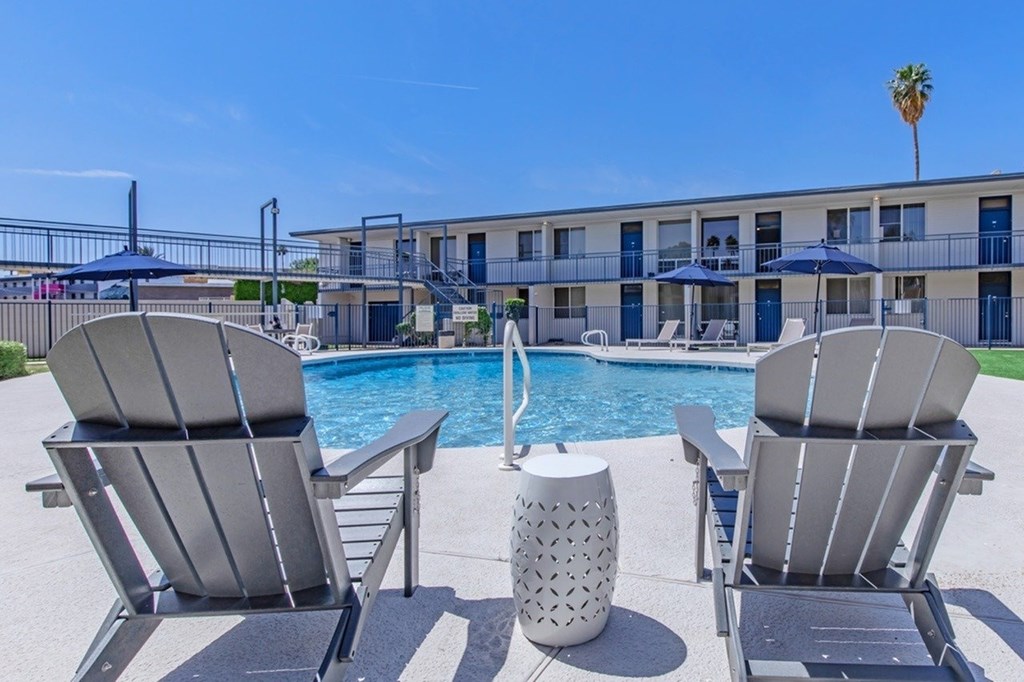 Two chairs are facing a pool with a building in the background.