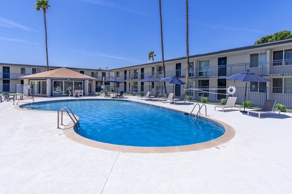 A swimming pool surrounded by a patio area with chairs and umbrellas.