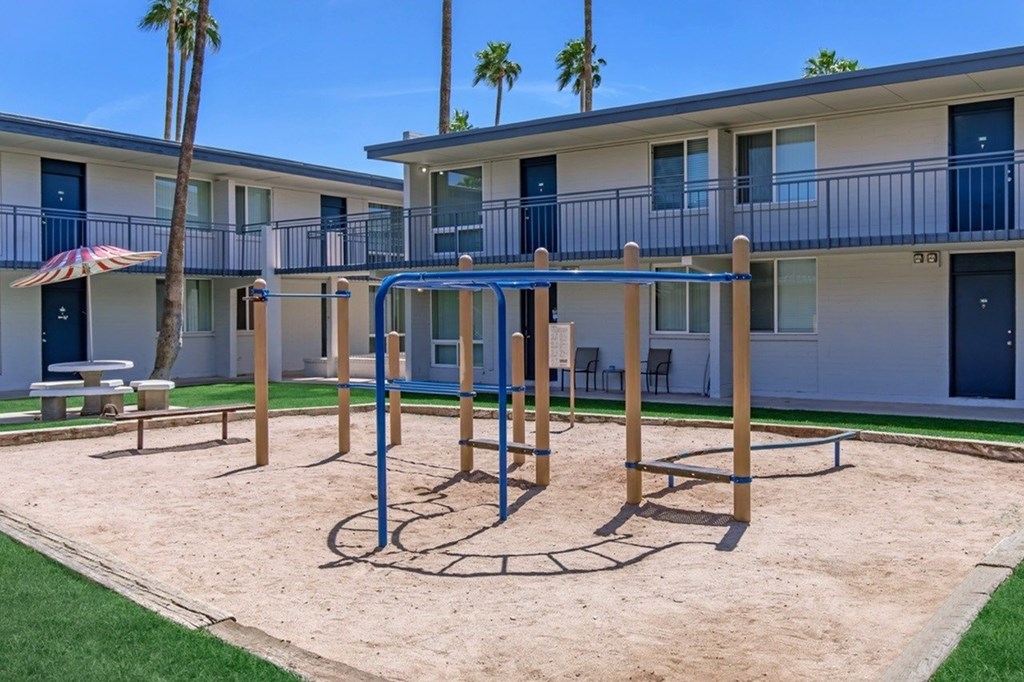 A playground with a swing set and a climbing frame in front of a building with balconies.