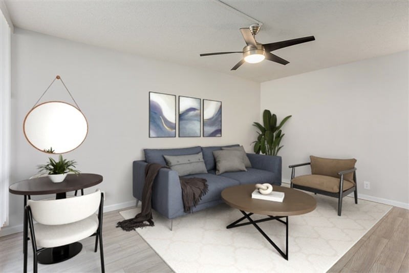 A living room with a grey couch, a brown armchair, a round table with a plant on it, and a painting on the wall.
