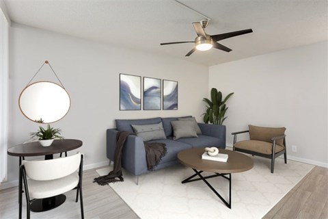 A living room with a grey couch, a brown armchair, a round table with a plant on it, and a painting on the wall.