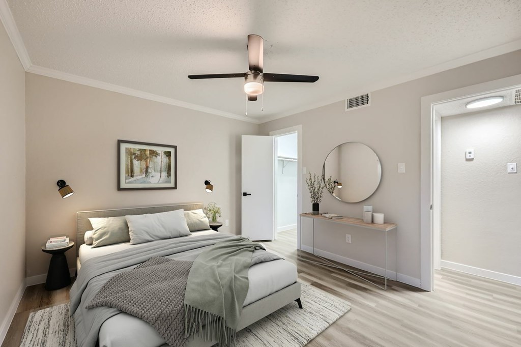 A bedroom with a bed, a nightstand, a side table, a mirror, and a ceiling fan.