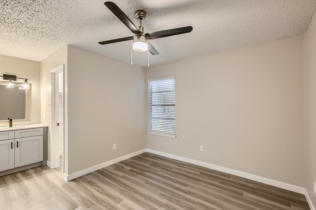 A room with a ceiling fan and light fixture, a window with blinds, and a wooden floor.