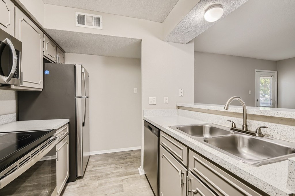 A kitchen with a black fridge and a stainless steel sink.