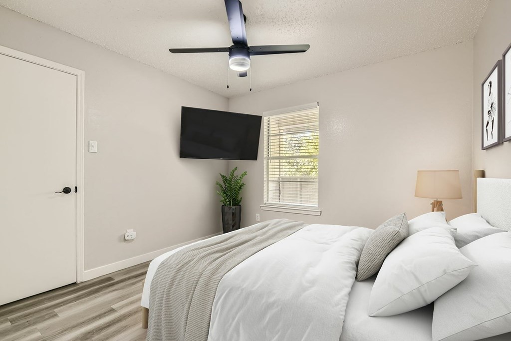 A bedroom with a bed, a ceiling fan, and a flat-screen TV mounted on the wall.